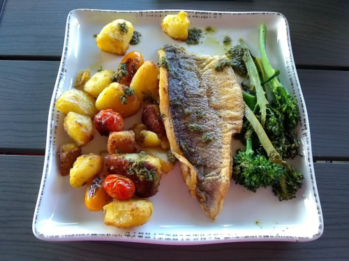 A plate of grilled fish with roasted potatoes, cherry tomatoes, and green beans, garnished with herbs.